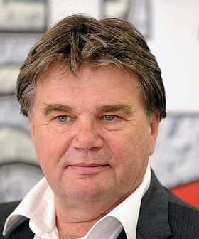 A man with short brown hair and blue eyes wearing a white shirt and dark suit jacket. - Olive Oil Times