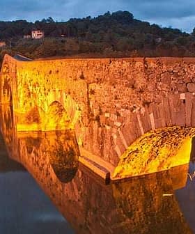 Stone bridge illuminated by warm light, reflecting in calm water during twilight. - Olive Oil Times