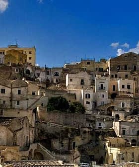 A view of historic stone buildings stacked on a hillside in Matera, Italy under a blue sky. - Olive Oil Times