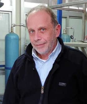 A man wearing a black jacket and a light blue shirt, standing in an industrial setting. - Olive Oil Times