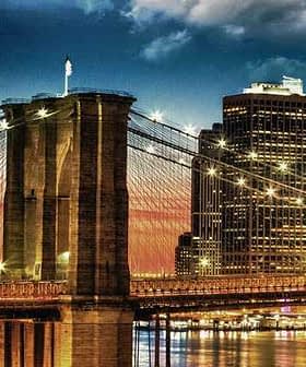 Brooklyn Bridge with illuminated towers and city skyline during sunset. - Olive Oil Times