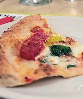 A slice of pizza topped with tomato sauce, cheese, spinach, and a yellow pepper on a white plate. - Olive Oil Times