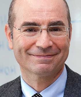 A man wearing glasses and a gray suit, smiling at the camera with a neutral background. - Olive Oil Times