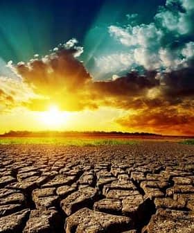 Dry, cracked earth with a vibrant sunrise and clouds in the background. - Olive Oil Times
