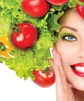 Woman with a hairstyle made of lettuce and tomatoes, smiling and posing with a hand on her face. - Olive Oil Times