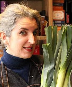Woman with gray hair holding a bunch of fresh leeks in a market setting. - Olive Oil Times
