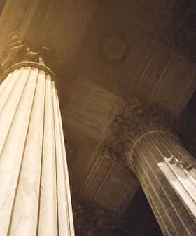 Two large architectural columns with intricate details and a view from below, showcasing their height and design. - Olive Oil Times