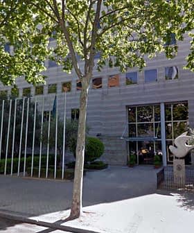 A modern office building with glass facade, surrounded by trees and parking spaces. - Olive Oil Times