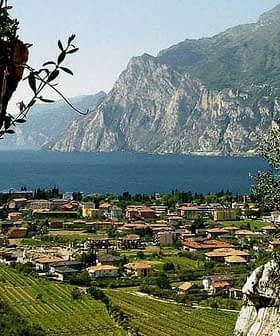 A scenic view of Lake Garda featuring mountains and a village with terracotta-roofed buildings. - Olive Oil Times