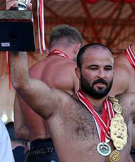Athlete celebrating victory by holding a trophy and wearing multiple medals at a competition. - Olive Oil Times