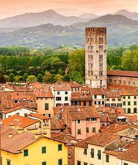Aerial view of Lucca's rooftops featuring a historic tower and surrounding mountains. - Olive Oil Times