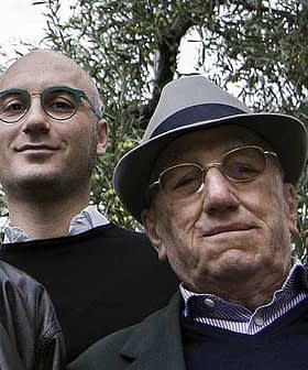 Two men standing together outdoors, one wearing glasses and a hat, the other with glasses and a dark sweater. - Olive Oil Times