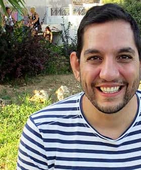 Man with short dark hair wearing a striped shirt, smiling at the camera outdoors. - Olive Oil Times