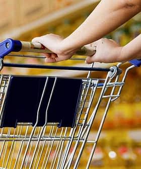 Close-up of a person's hand holding the handle of a shopping cart in a store. - Olive Oil Times