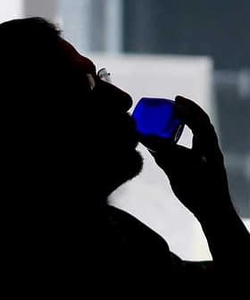Silhouette of a person holding a blue glass to their lips while drinking. - Olive Oil Times