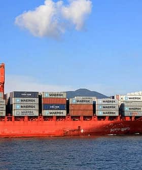Red cargo ship loaded with shipping containers, including Maersk branding, on the water. - Olive Oil Times