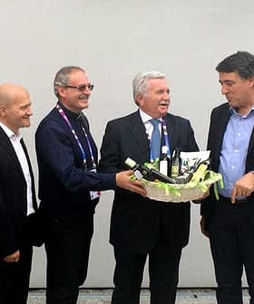 Four men standing together, one presenting a basket filled with olive oil products. - Olive Oil Times