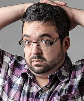 Man with glasses and a plaid shirt holding his head with both hands, looking surprised. - Olive Oil Times