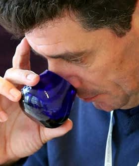 Man holding a blue glass cup and smelling the contents while tasting olive oil. - Olive Oil Times