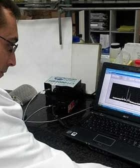 A scientist in a lab coat examining data displayed on a laptop screen in a laboratory setting. - Olive Oil Times