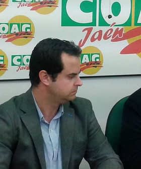 Three men seated at a table during a press conference with COAG branding in the background. - Olive Oil Times