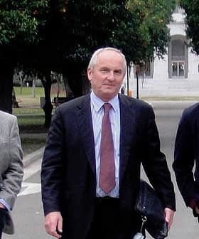 Three men walking together in a park, carrying briefcases and folders. - Olive Oil Times