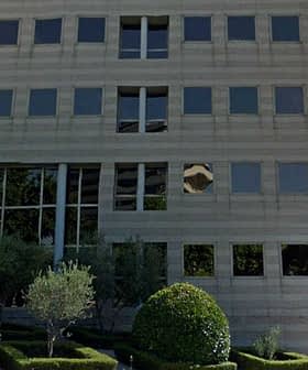 Contemporary office building featuring large glass windows and a landscaped area. - Olive Oil Times