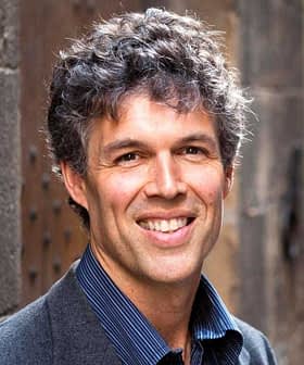 A man with curly hair and a friendly smile, wearing a dark blazer and blue shirt. - Olive Oil Times