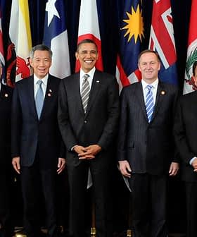 Group of ten political leaders posing for a photo at an international summit with flags in the background. - Olive Oil Times