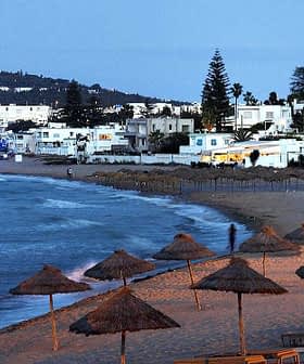 Coastal view featuring beach umbrellas and white buildings along the shoreline at dusk. - Olive Oil Times