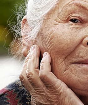 Elderly woman with gray hair and a thoughtful expression, resting her chin on her hand. - Olive Oil Times