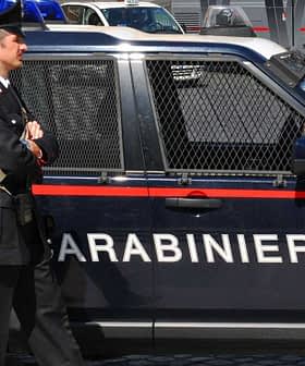 A Carabinieri officer standing next to a marked police vehicle in an urban setting. - Olive Oil Times