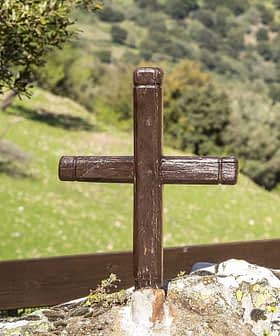 A wooden cross placed on a rock in a natural outdoor setting with greenery in the background. - Olive Oil Times