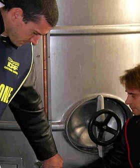 Two inspectors in vests examining olive oil storage tanks in a facility. - Olive Oil Times