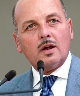 Man in a gray suit speaking into a microphone at a podium during an event. - Olive Oil Times