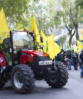 Red tractor surrounded by yellow flags at a demonstration in an urban area. - Olive Oil Times
