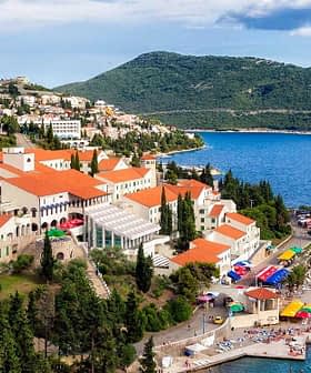 A coastal view of a Mediterranean town with red-roofed buildings and a blue sea. - Olive Oil Times