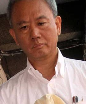 A man in a white shirt being escorted by two police officers outside a building. - Olive Oil Times