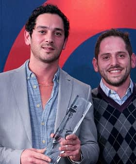 Four men standing together, one holding an award, in a formal setting with a colorful background. - Olive Oil Times