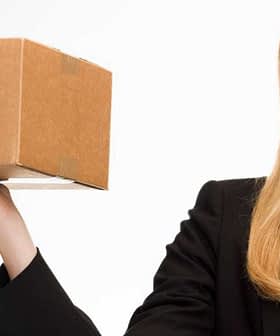 A woman in a black blazer holding a cardboard package with marketplace branding. - Olive Oil Times