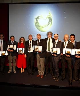Group of individuals holding awards during a ceremony with a backdrop display. - Olive Oil Times