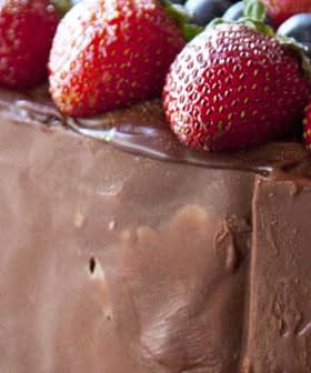 Chocolate cake topped with strawberries and blueberries, surrounded by rose petals. - Olive Oil Times