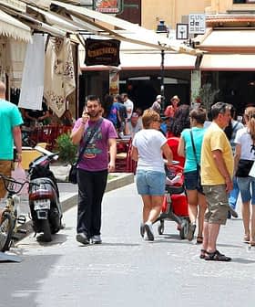 People walking and shopping in a market street with various shops and stalls. - Olive Oil Times