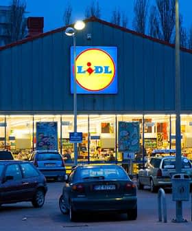 Exterior view of a Lidl supermarket with a lit sign and parked cars in front during dusk. - Olive Oil Times