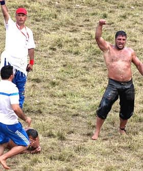 Competitors in a Turkish oil wrestling match with one wrestler celebrating a victory in a grassy field. - Olive Oil Times