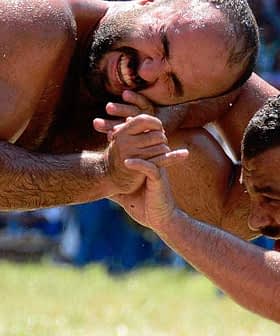 Two male wrestlers in a Greco-Roman wrestling match, grappling on a grassy field. - Olive Oil Times