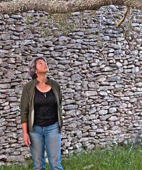 Two individuals looking up at a tree branch in front of a stone wall. - Olive Oil Times