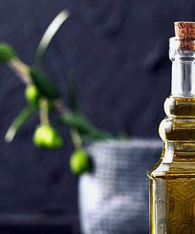 A glass olive oil cruet with a cork stopper, featuring a smooth design and filled with olive oil. - Olive Oil Times
