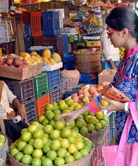 A woman selecting limes from a basket in a busy fruit market with people around her. - Olive Oil Times