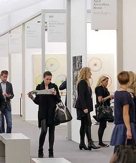 People walking through an art gallery exhibition with various artworks displayed on the walls. - Olive Oil Times